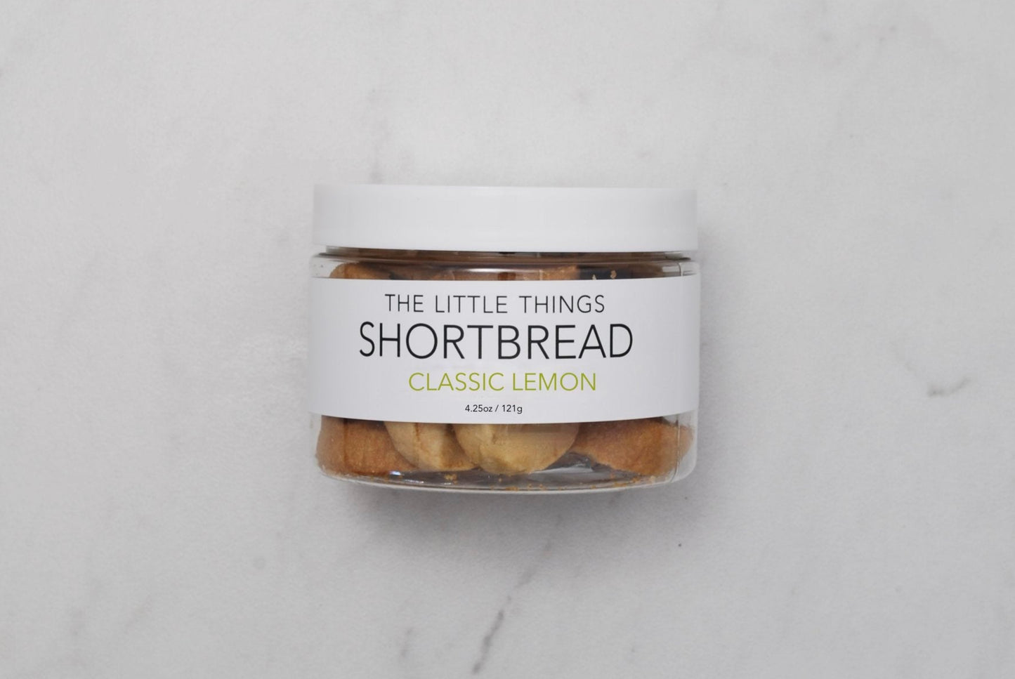 A jar of lemon shortbread cookies on a marble surface.